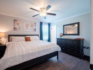 A bedroom with a bed, a dresser, a ceiling fan, and artwork on the wall.