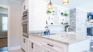 A modern kitchen with white cabinetry, stainless steel appliances, and pendant lighting.