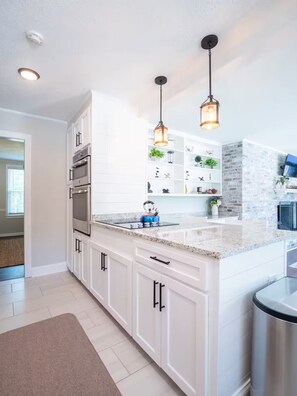 A modern kitchen with white cabinetry, stainless steel appliances, and pendant lighting.