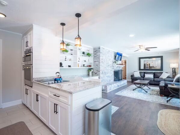 Una cocina moderna con armarios blancos, encimera de granito e iluminación colgante.