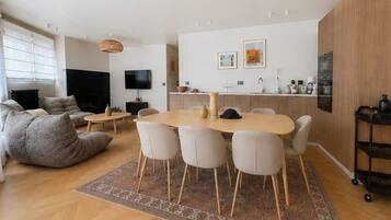 A modern living room with a sofa, a coffee table, a TV, and a dining area with a table and chairs.
