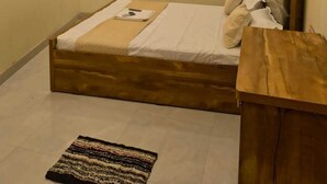 Un dormitorio con una cama, cabecera de madera, mesita de noche, televisor montado en la pared y una alfombra pequeña.