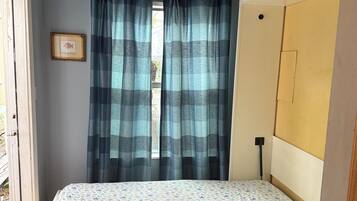 A bedroom with a bed, a ceiling fan, a window with curtains, and an air conditioning unit.