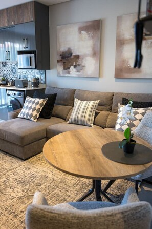 A modern living room with a sectional sofa, a round coffee table, and abstract wall art. - Slick Studio at Ocean Club H24 (Ballito)
