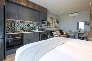 Eine moderne Küche mit Backofen von Bosch, einer Mikrowelle und einer Waschmaschine. Ein Bett mit grauer Decke und ein Sofa mit gemusterten Kissen.