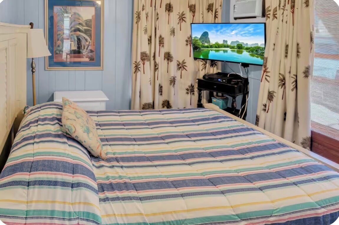 A hotel room with a bed, a television, a desk with a computer, and a window with curtains.