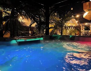 Ein Innenpool mit Whirlpool, umgeben von Palmen und stimmungsvoller Beleuchtung.