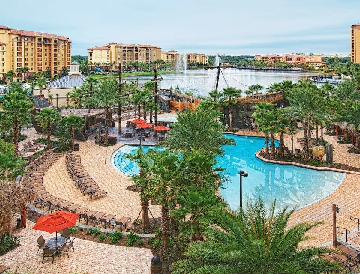 Un resort con una piscina grande, palmeras y una fuente de agua.
