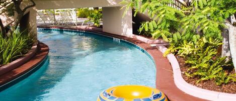 A swimming pool with a yellow inflatable ring, surrounded by plants and a covered area with lounge chairs.