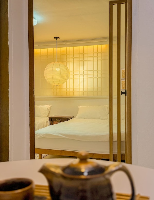 Une chambre avec un lit, une table de chevet, une lampe classique et une table en bois sur laquelle se trouve une théière.