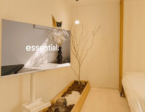 A hotel room with a bed, a bedside table with a vase of flowers, a TV mounted on the wall, and a small wooden planter with a tree branch. - Jamil station 10 mind. 9 line subway station. Lottery world tower (Seoul)