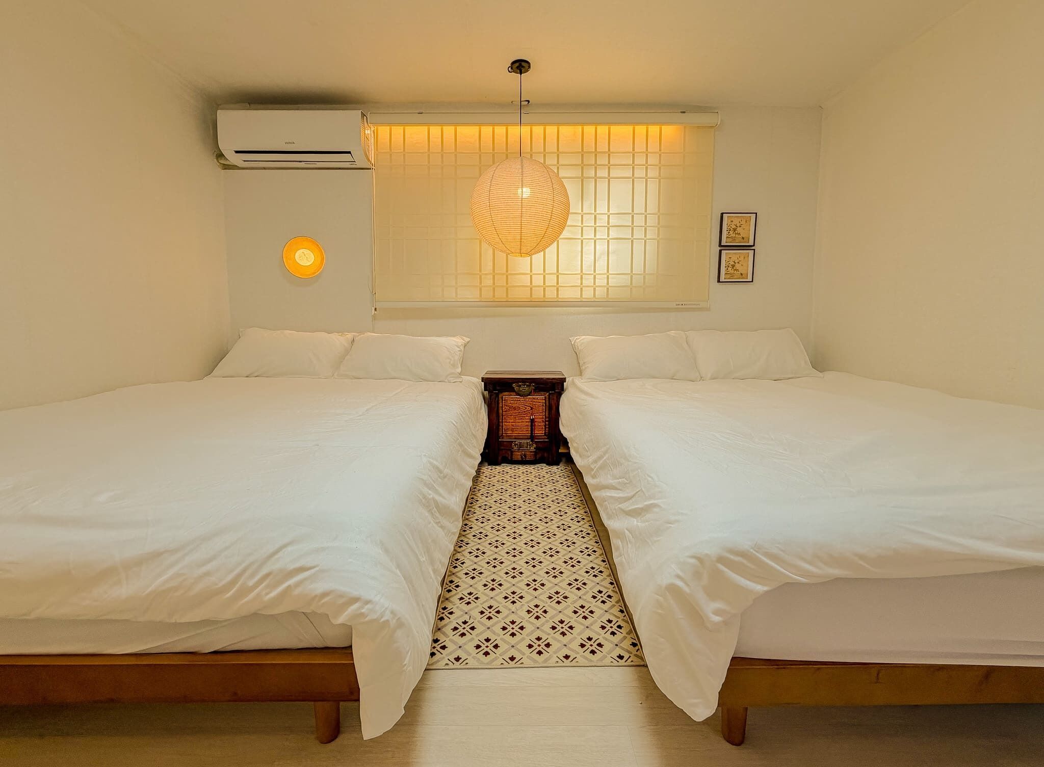 A double bed room with a central rug, a wall-mounted air conditioner, and a hanging light fixture.
