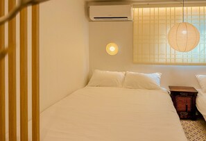 Ein Zimmer mit einem Bett, einer Wandklimaanlage, einer Hängelampe und einem Fenster mit Gittermuster.