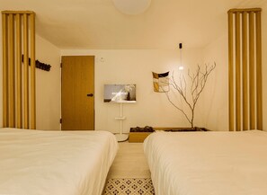 Une chambre d’hôtel avec deux lits, une télévision, une petite table avec un vase et une branche décorative.