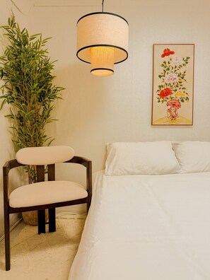 A bedroom with a bed, a chair, a hanging light fixture, a potted plant, and a framed floral artwork on the wall. - Jamil station 10 mind. 9 line subway station. Lottery world tower (Seoul)
