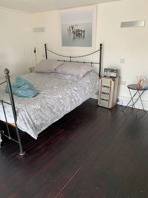 A bed with a metal frame, a bedside table with a radio, and a small round table with a vase. - The Cabin At The Beach (Seasalter)