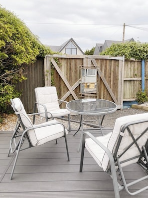 A deck with a glass-top table and four white cushioned chairs. - The Cabin At The Beach (Seasalter)