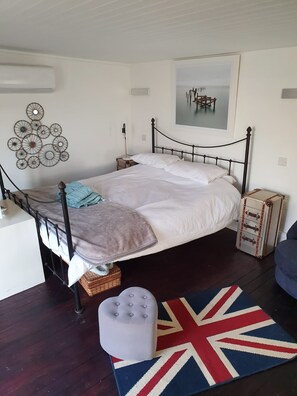 A neatly arranged bedroom with a single bed, bedside tables, a wall art piece, a suitcase, and a British flag rug. - The Cabin At The Beach (Seasalter)