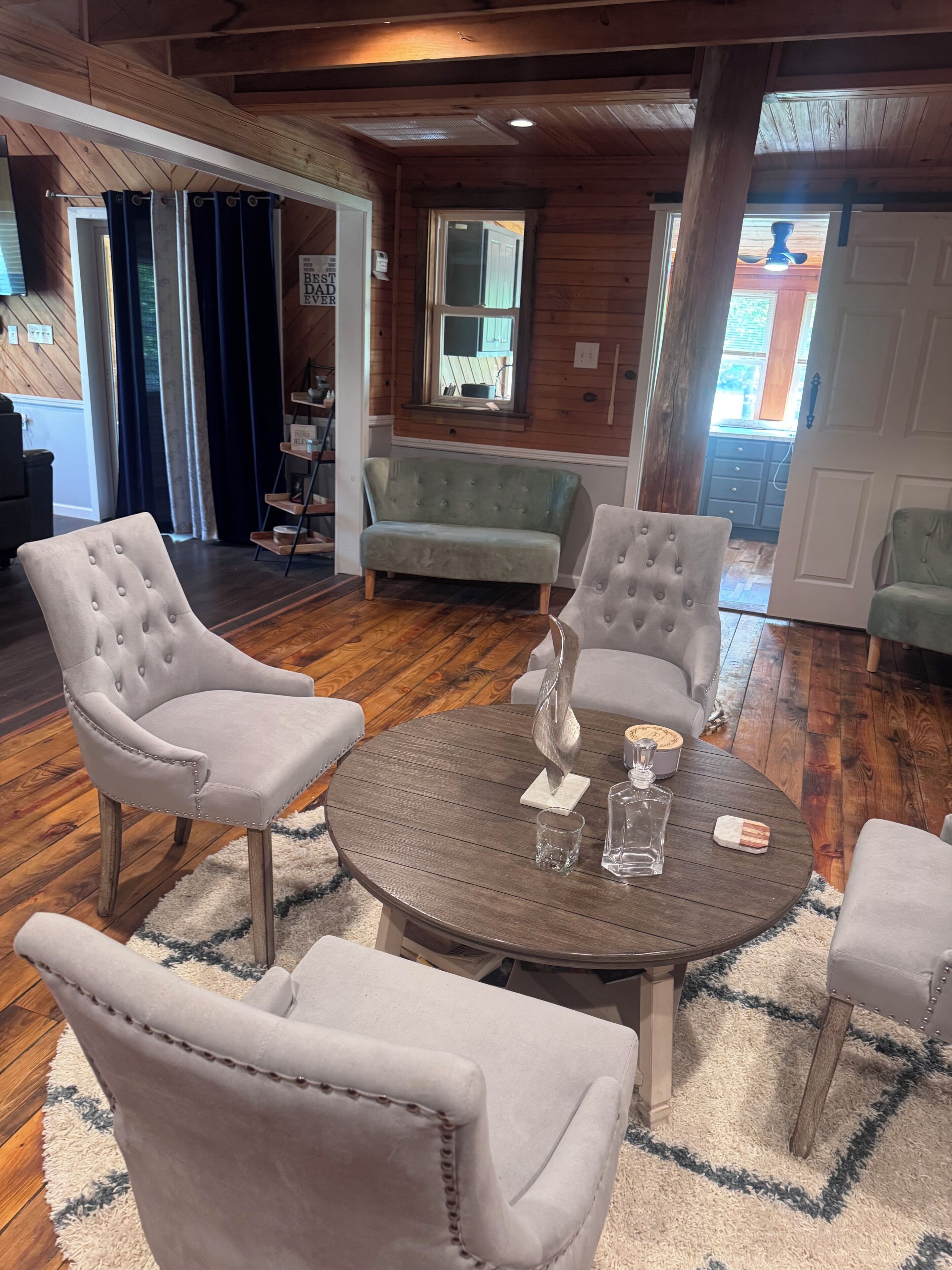 A room with a round wooden table, four upholstered chairs, a sofa, and a window with a view.