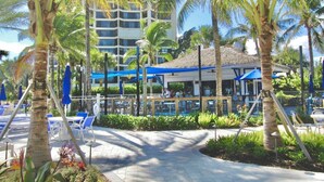 Ein Resort mit Poolbereich, Palmen und einem Gebäude mit blauem Markisenvorzelt.