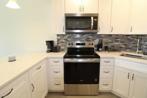 A modern kitchen with white cabinets, a stainless steel microwave, a built-in oven, and a coffee maker. - Seabreeze - Beautiful Newly Renovated 2 Bed Condo - Oceanfront Community - Golf Course - Resort Pool (Fort Pierce)