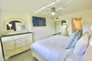 Una camera da letto con un letto, una cassettiera, una ventola a soffitto e un quadro appeso al muro.