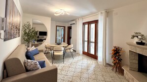 A living room with a sofa, a dining table with chairs, a fireplace, and a large mirror.