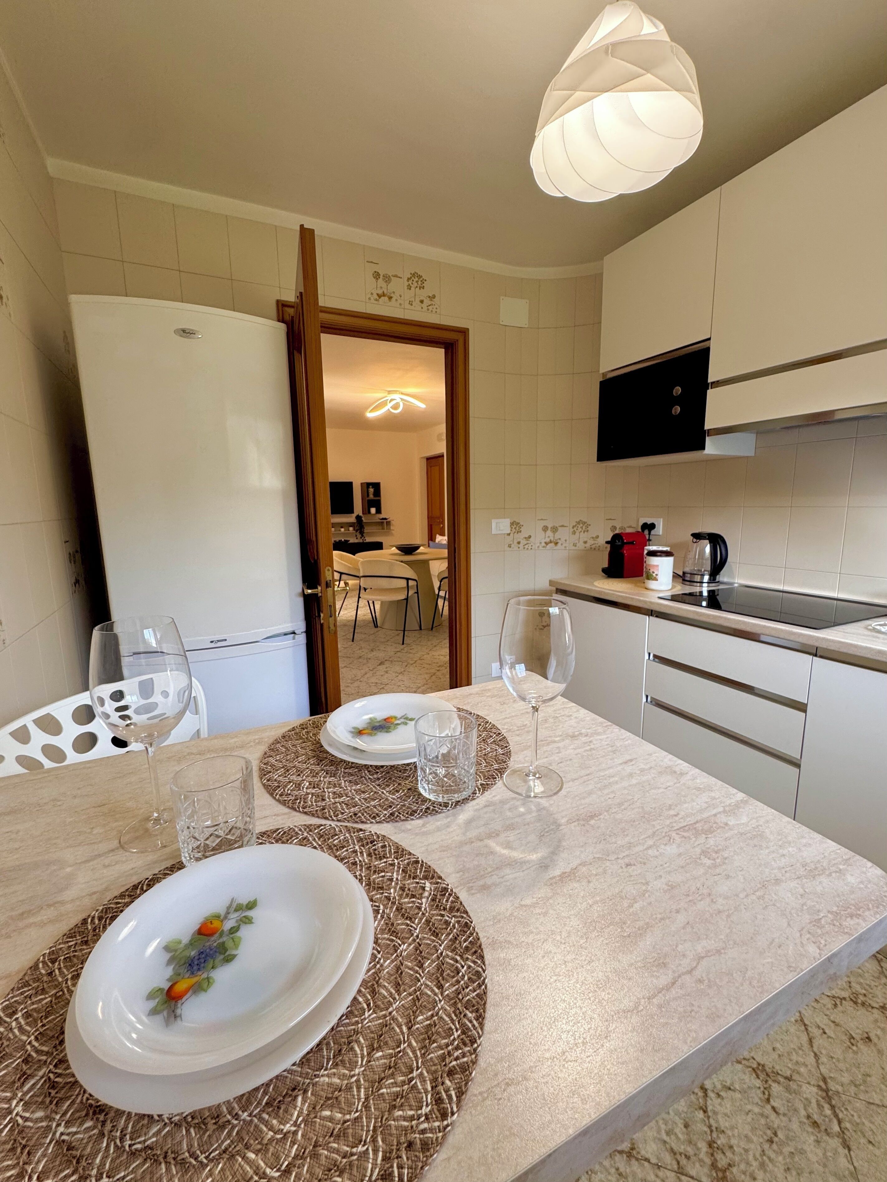 Una cocina moderna con comedor, que incluye un refrigerador, una cafetera y una mesa de comedor con platos y vasos.