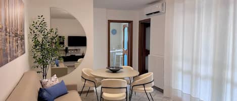Una sala de estar moderna con un sofá, una mesa de comedor con sillas, una planta en maceta y un televisor.
