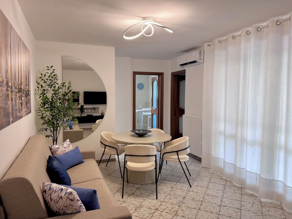 Un salon moderne avec un canapé, une table à manger et des chaises, une plante en pot et un téléviseur.