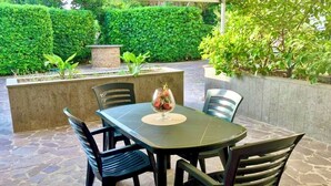 An outdoor patio with a table and chairs, surrounded by stone flooring and greenery.