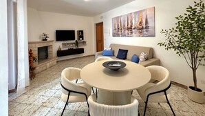 A modern living room with a round table, white sofas, a flat-screen TV, and a fireplace.
