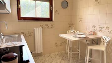 A kitchen with a sink, a window, a clock, and a dining area with chairs and a table.