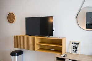 Ein modernes Zimmer mit einem Flachbildfernseher auf einem hölzernen TV-Schrank, einer Wanduhr, einem gerahmten Bild und einem kleinen Tisch mit einer Fernbedienung.
