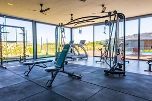 Ein modernes Fitnessstudio mit verschiedenen Trainingsgeräten, großen Fenstern und Blick ins Freie.