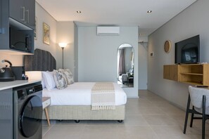 A modern hotel room with a bed, a desk, a washing machine, a TV, and a mirror. - Gorgeous Ocean Club Studio G21 (Durban)