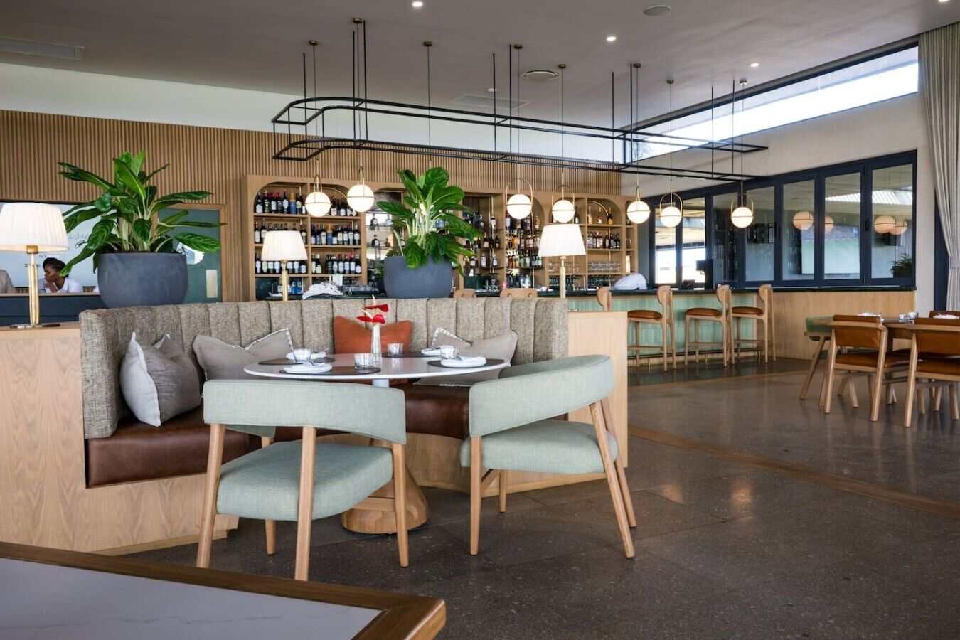A modern restaurant interior with a bar area, seating arrangements, and a view of the outside.