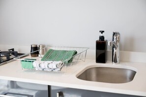 Eine Küche mit Spüle aus Edelstahl, einem Geschirrgestell mit zusammengelegten Handtüchern, einer Seifenspender und einem Wasserkocher.