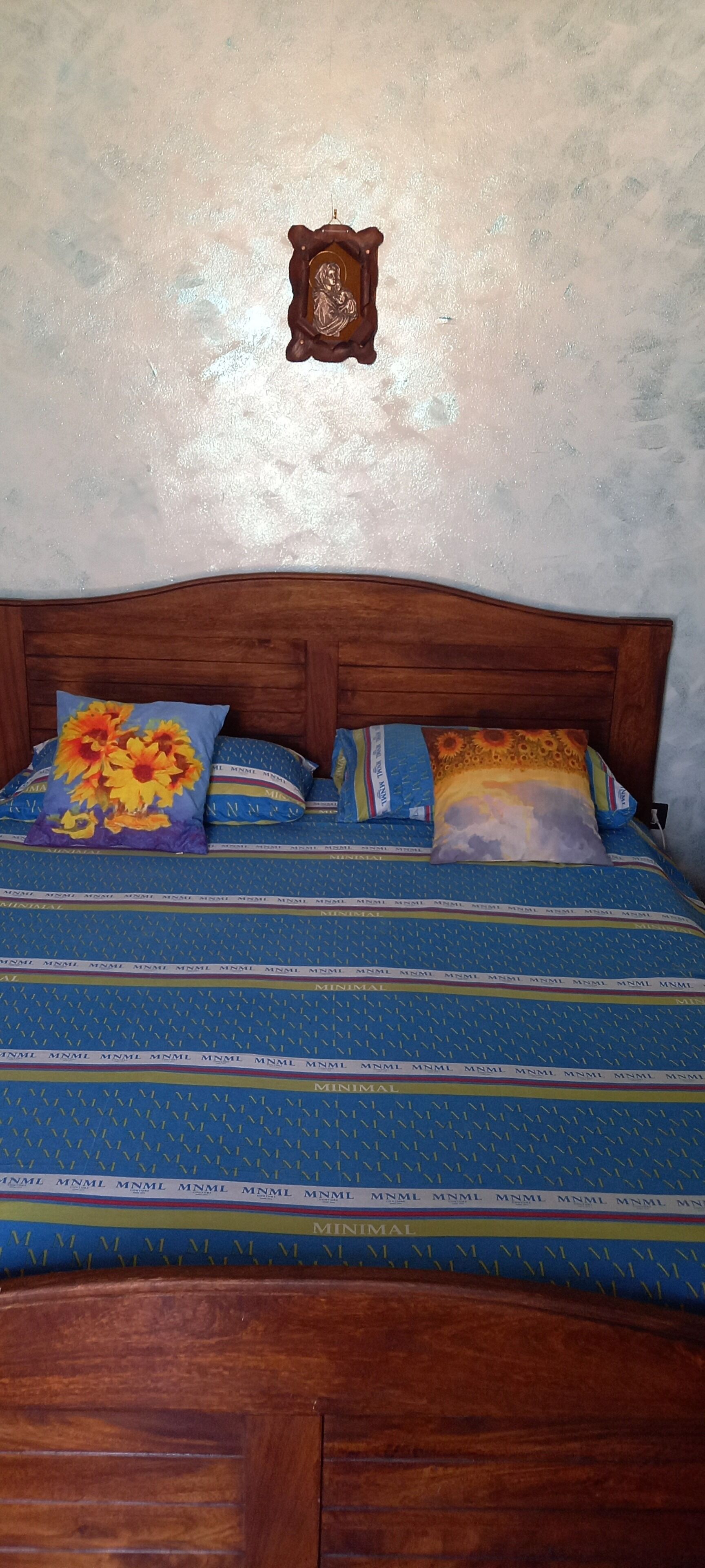 A bed with a wooden headboard, blue bedding with 'MINIMAL' text, and floral-patterned pillows.