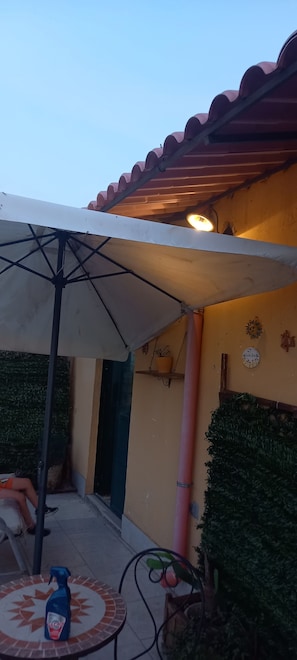 Ein Terrassenbereich im Freien mit Tisch und Stühlen, einem Sonnenschirm und einer Wand mit dekorativen Elementen.