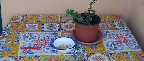Un patio con baldosas, una planta en maceta, una mesa pequeña y un macetero colgante.