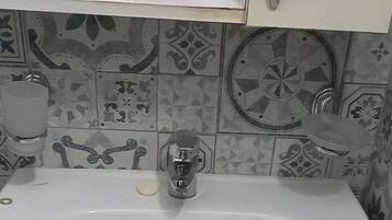 Une salle de bain avec un lavabo blanc, un miroir et des articles de toilette posés sur le comptoir.