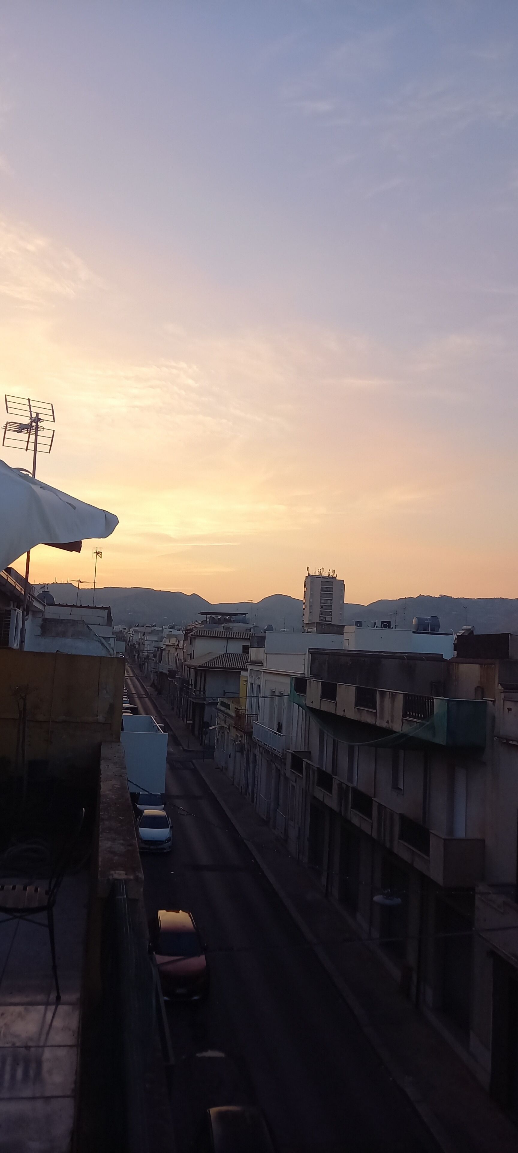 Una vista di strada con edifici, un'auto parcheggiata e cielo sereno.