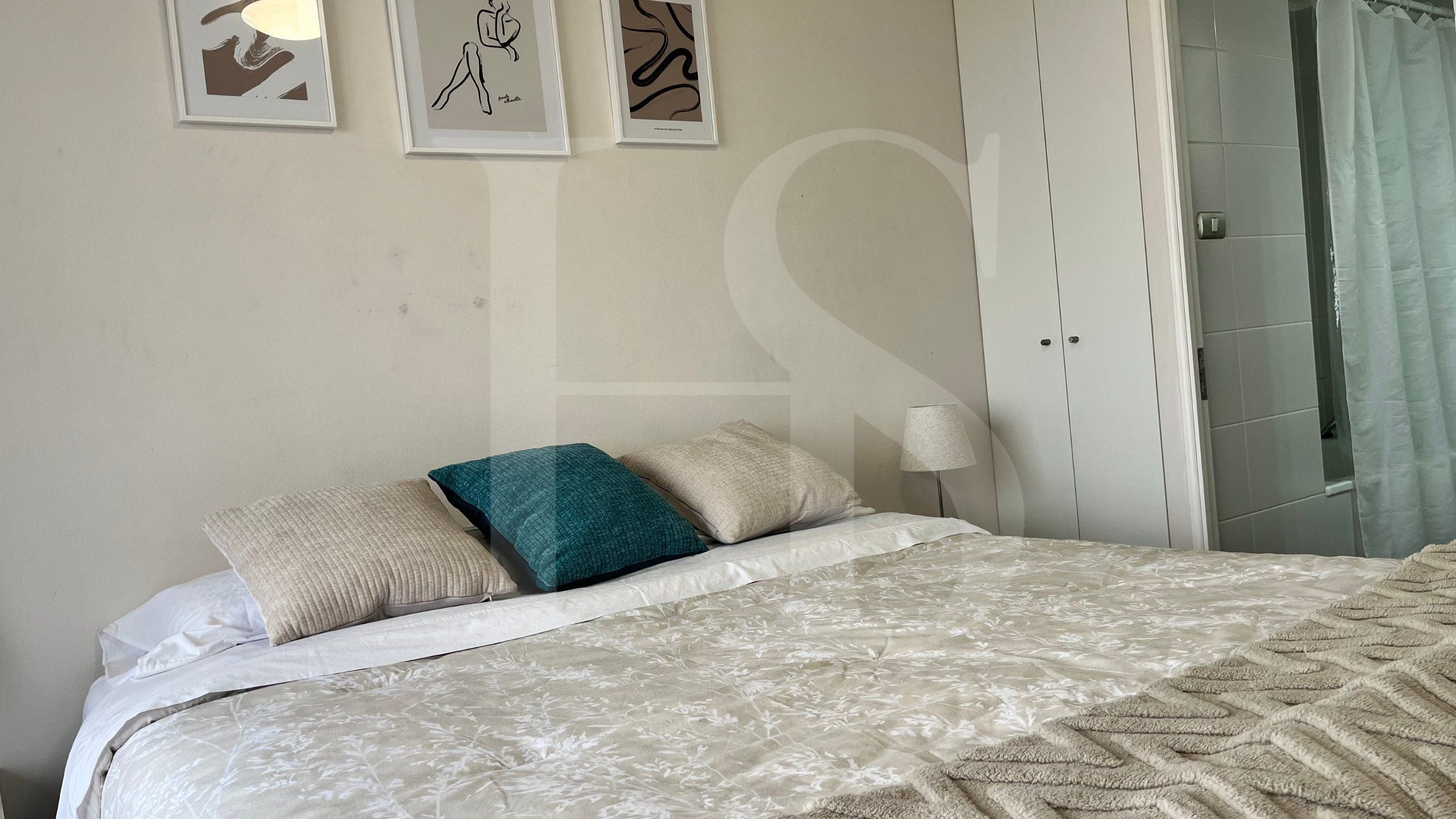 Un dormitorio con cama, almohadas, una mesita de noche y una puerta que da al baño.