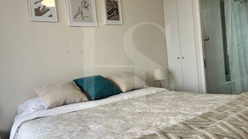 Un dormitorio con cama, almohadas, una mesita de noche y una puerta que da al baño.
