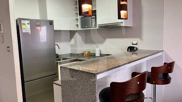 Una cocina moderna con refrigerador de acero inoxidable, encimera de granito y dos taburetes de madera.