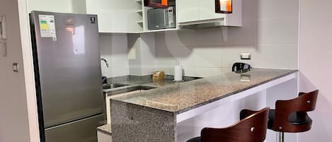 A modern kitchen with a stainless steel refrigerator, granite countertop, and two wooden bar stools.