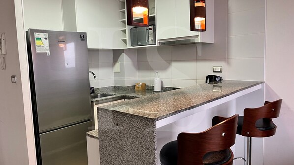 A modern kitchen with a stainless steel refrigerator, granite countertop, and two wooden bar stools.