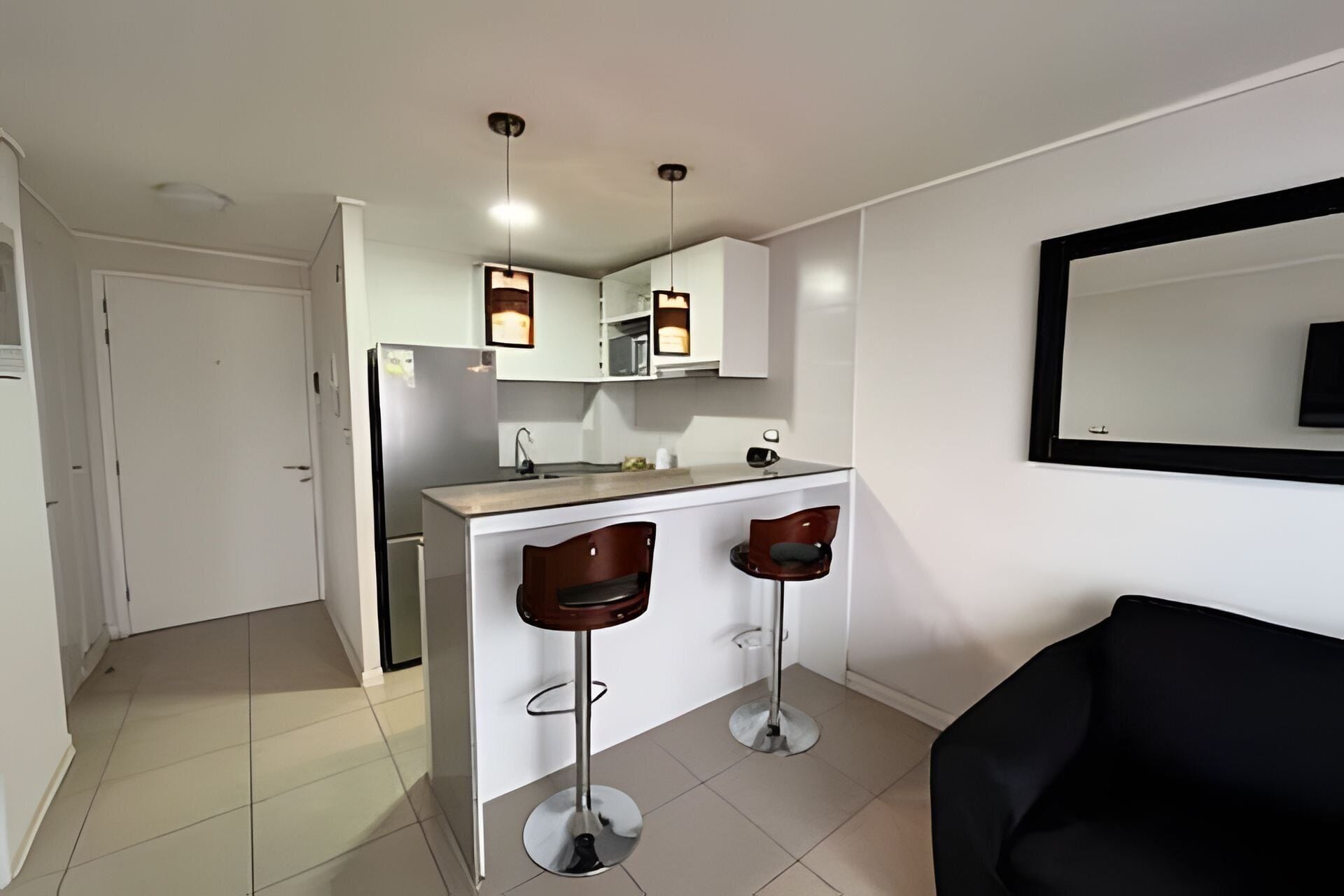 Una cocina compacta con refrigerador, un lavamanos y dos taburetes de bar.