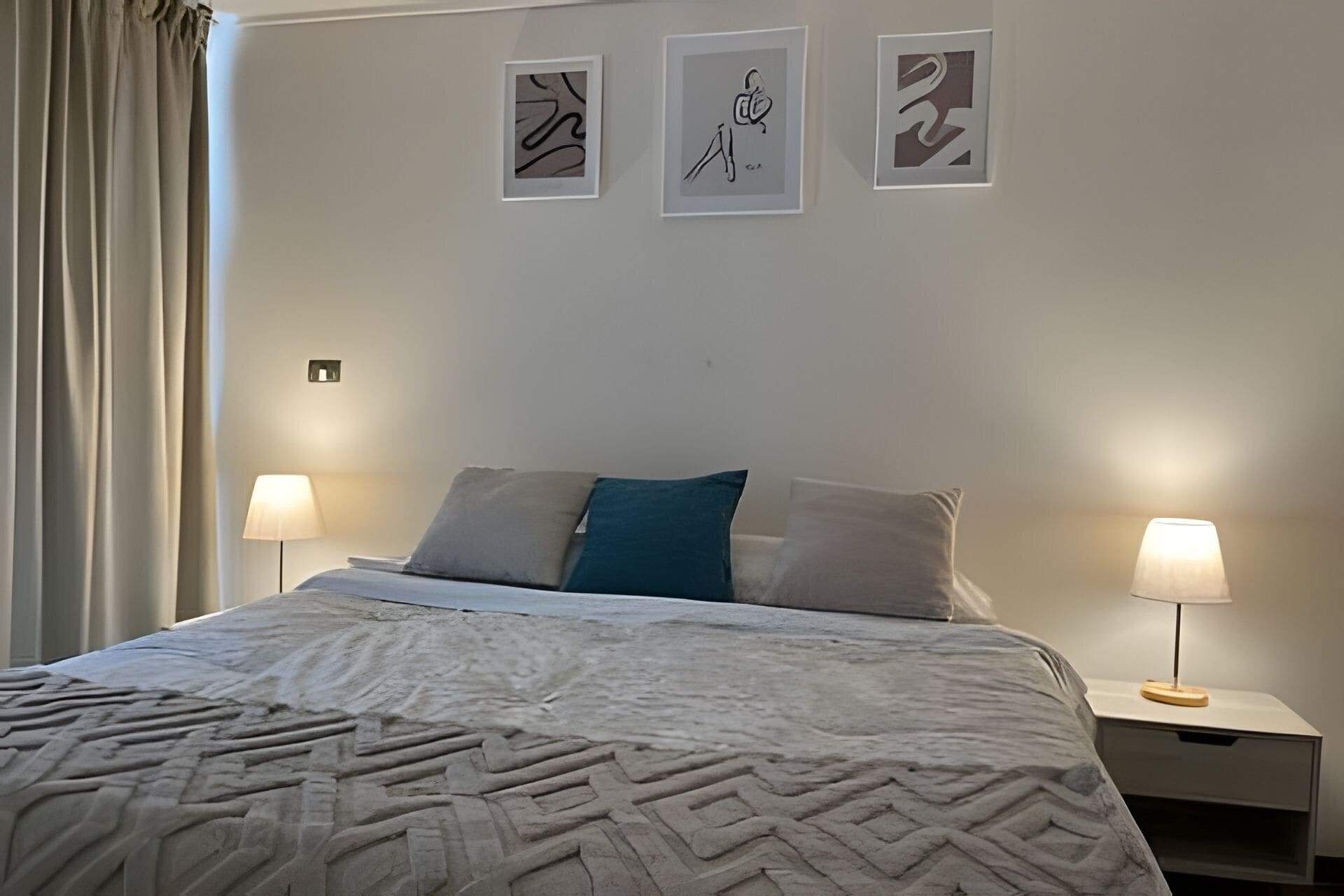 Una habitación de hotel con una cama, dos lámparas de noche y tres obras de arte enmarcadas en la pared.